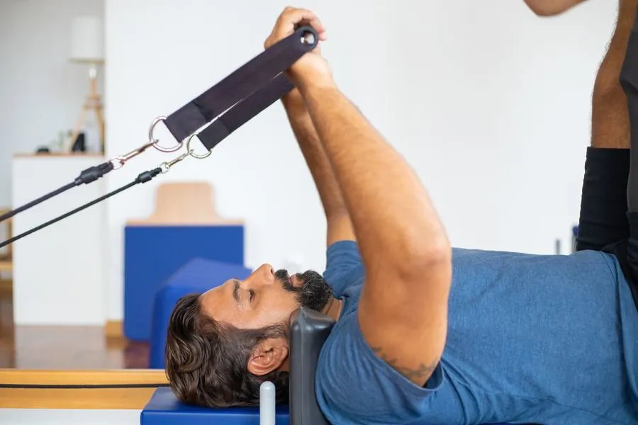 A man on a reformer pulling a strap overhead