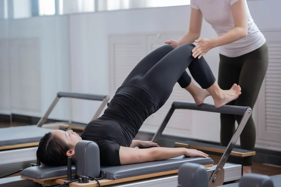 A teacher guiding a client's leg on a reformer
